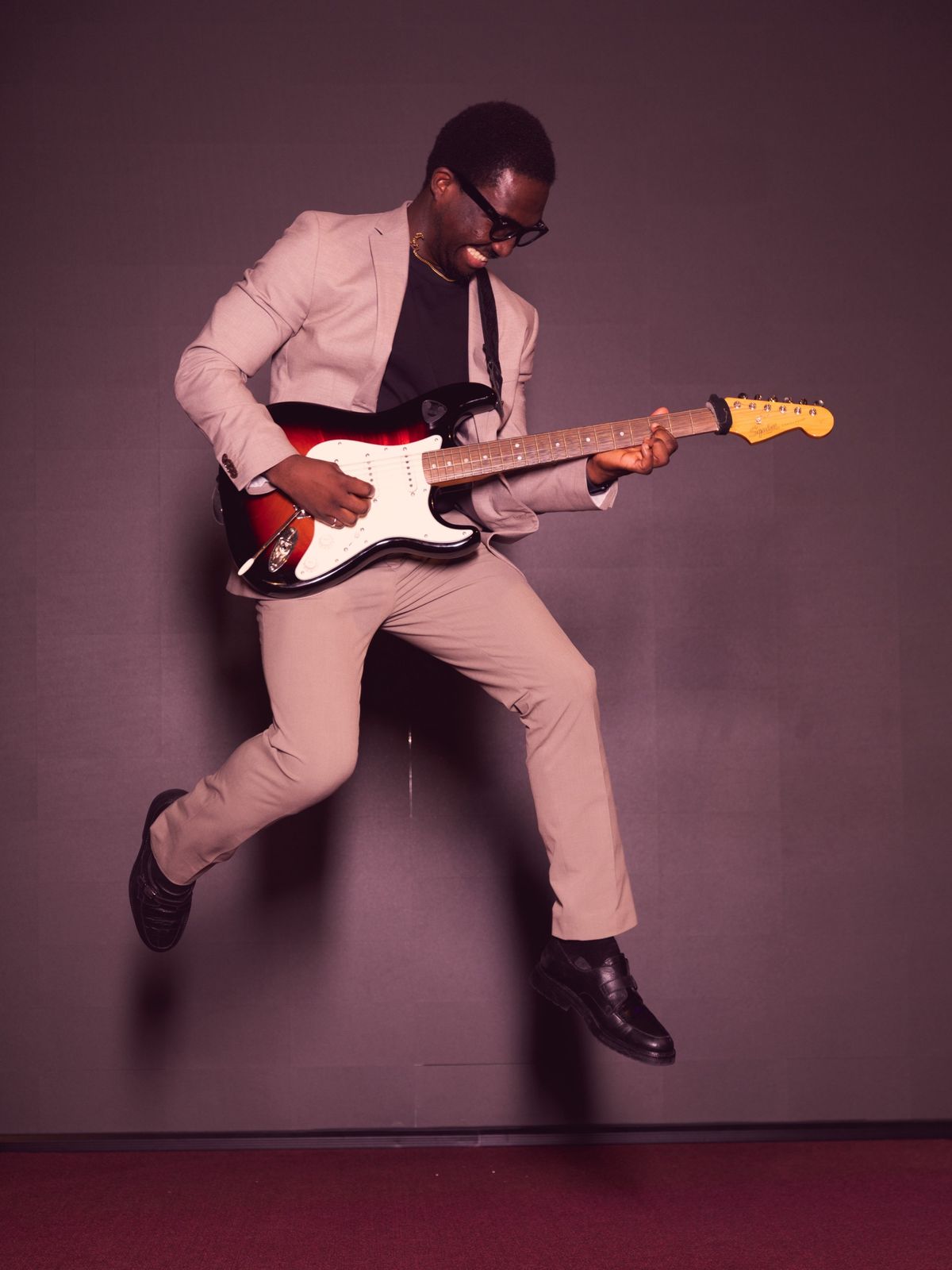 Divine mid-jump in a beige suit, playing an electric guitar